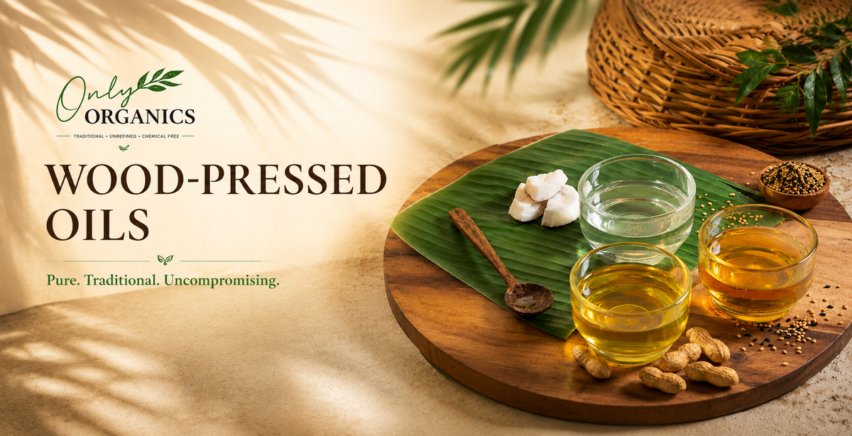 Promotional graphic for Only Organics Wood-Pressed Oils, showing three glass cups filled with golden oil on a round wooden tray, alongside peanuts, a spoon, garlic cloves, and a banana leaf. The left side features a beige background with palm leaf shadows and the product branding text.